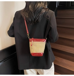 Detail view of woven straw bucket bag with burgundy leather trim and long shoulder strap