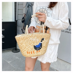 Detail of hand-woven straw tote bag with Hola embroidery and a rounded handle design