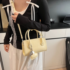 Detail of cream yellow mini Boston bag with heart charm and brand logo on shoulder strap