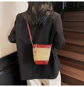 Detail of straw woven bucket bag featuring red leather trim and golden metal hooks