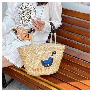 Close-up of woven straw bag featuring swan embroidery and a Hello text design