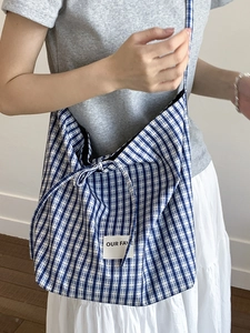 Blue and white checkered canvas tote bag with Our Fave logo shown on a model