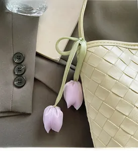 Detail of a beige woven bucket bag featuring a purple tulip floral charm attachment