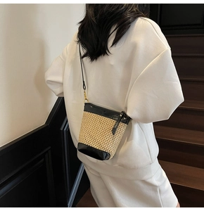 Detail of a straw crossbody bucket bag with black leather trim and golden hardware