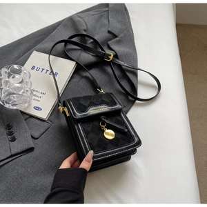 Detail of black leather crossbody bag with diamond quilting and gold hardware on grey suit