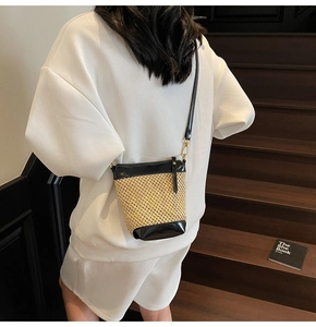 Model wearing a woven straw bucket bag with black leather trim on wooden stairs