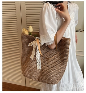 Detail of woven straw tote bag with white lace bow and brown leather handles