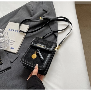 Detail of black patchwork crossbody phone bag with gold metal pendant and refined texture