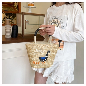 Detail of hand-woven straw tote bag with duck embroidery and Hola text for summer beach