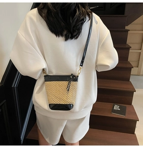 Detail of hand-woven straw bucket bag with black leather trim and elegant gold hardware