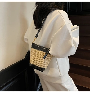 Detail of straw bucket bag with black leather trim worn over a white casual outfit