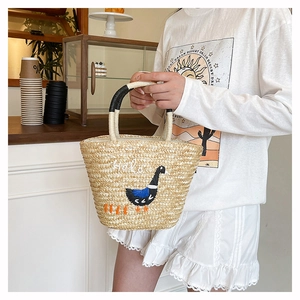 Detail of straw woven tote bag featuring Hola embroidery and a black duck pattern
