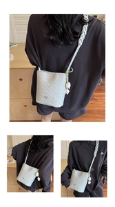 Detail of mint green woven crossbody bag with tulip charm and braided strap detail