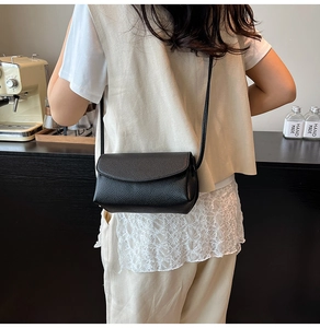 Détail d'un sac à bandoulière en cuir noir à texture litchi porté par un mannequin
