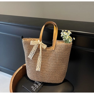 Detail of woven straw tote bag with brown leather handles and decorative white lace bow