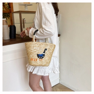 Detail of hand-woven straw tote with black swan embroidery and Hola text