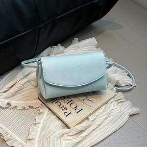 Détail de la texture en cuir grainé bleu clair et du rabat rectangulaire sur le sac