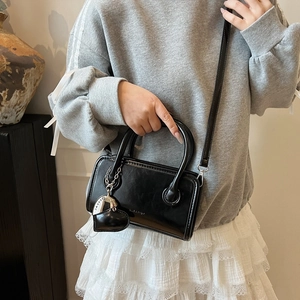 Detail of black bowling handbag with heart charm and shoulder strap on model