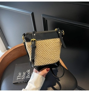 Detail of straw woven bucket bag with black leather trim and gold zipper closure