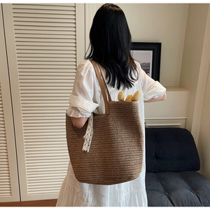 Close-up of caramel woven straw tote with leather straps and delicate lace ribbon detail