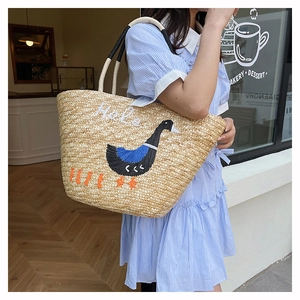Detail of handwoven straw tote bag featuring a cute goose embroidery and white rope handle
