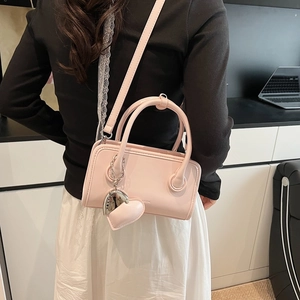Pink bowling style handbag with heart charm detail shown in a model back view