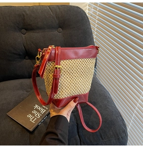 Detail view of woven straw bucket bag with reddish-brown leather trim and metal buckles