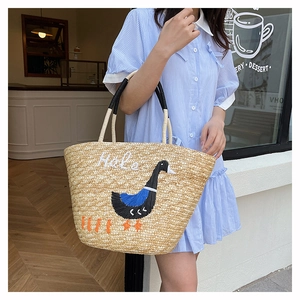 Detail of hand-woven straw tote bag with Hola embroidery and blue goose design