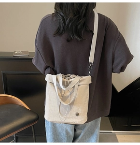 Detail of beige drawstring tote bag with shoulder strap worn by a model in casual style
