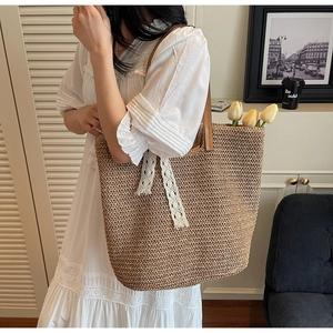 Detail of woven straw tote bag with brown leather straps and white lace ribbon decoration