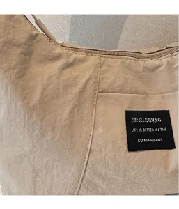 Dettaglio della borsa tote in nylon beige con trama a pieghe, cerniera ed etichetta in tessuto