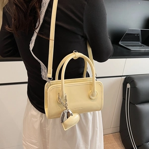Detail view of cream-colored bowling bag with heart charm and crossbody strap