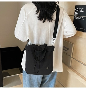Detail of a black minimalist tote bag with metal logo and drawstring worn as a crossbody