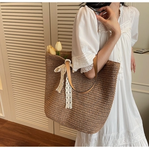 Detail of woven straw tote bag featuring white lace bow decoration and leather shoulder strap