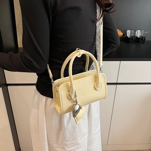 Detail of cream yellow PU leather mini bowler bag with heart-shaped metal charm and handles