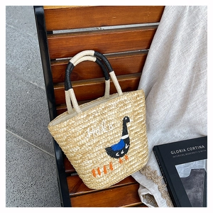 Detail view of woven straw tote bag with swan embroidery and contrast wrapped handles