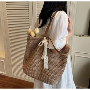 Detail of woven straw tote bag with brown leather straps and elegant lace ribbon decoration