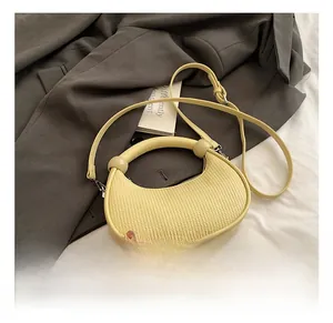 Detail of pale yellow crescent handbag with unique spherical decorative handle on grey fabric