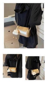Detailansicht der goldmetallic Zylindertasche mit einem niedlichen weißen Plüschwolken-Anhänger