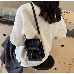 Side view of black crossbody mini bag with diamond quilting and gold buckle on a model