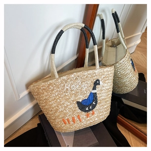 Detailed close-up of straw tote bag with cartoon bird embroidery and Hello lettering