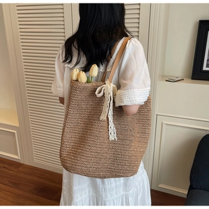 Detailed back view of a straw tote bag with brown leather straps and white lace bow decoration