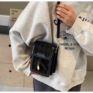 Close-up of black quilted cell phone crossbody bag with gold metal logo and round pendant
