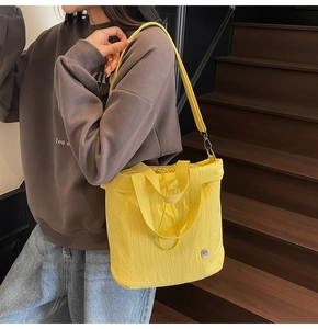 Detail of yellow tote bag with crinkled texture, drawstring and round metal logo