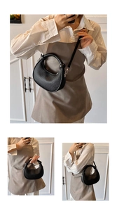 Detail view of black pleated crescent handbag with ring handle and detachable strap