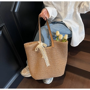 Detail of hand-woven straw tote bag with brown leather handles and white lace bow