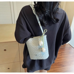 Detail showing light blue woven leather bucket bag with white tulip charm on shoulder