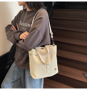 Detailed view of cream nylon tote bag worn over shoulder on wooden stairs