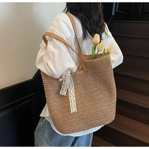 Detail of woven straw tote bag with brown leather straps and white lace ribbon decoration