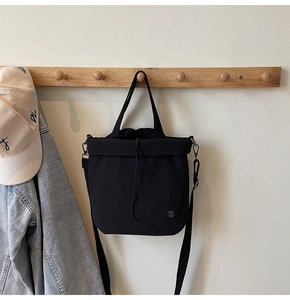 Detail of minimalist black drawstring tote bag with M logo hanging on a wooden hook